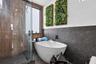 Freestanding soaking tub featuring matte black wall-mounted fixtures, vertical wood-slat accent wall, glass-enclosed shower, and large-format tile wal