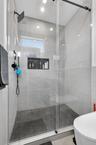 Walk-in shower featuring large-format light grey wall tile, a textured pebble-style floor, a built-in recessed niche, a frameless glass enclosure, and
