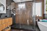 Walk-in shower featuring a frameless glass enclosure, floor-to-ceiling slatted wood-finish wall panels, large-format dark tile surround, and a freesta