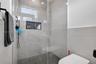 Walk-in shower featuring large-format stone-finish tile surround, integrated recessed storage niche, pebble-textured flooring, frameless glass enclosu