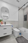 Bathroom featuring a white wall-mounted vanity with black hardware, an oval mirror, a tub-shower combination with a glass sliding enclosure, and large