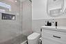 Walk-in shower with frameless glass enclosure, built-in tiled niche, white vanity with rectangular sink, matte black faucet, and oval wall-mounted mir