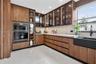 Wood-finish cabinetry with glass-front display panels, integrated double wall ovens, stone-finish countertops, matte black apron-front sink, and polis