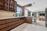 Modern kitchen featuring wood-finish cabinetry, stone countertops, a deep farmhouse-style sink, glass-front upper cabinetry with integrated lighting, 