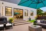Patio area featuring light-toned tile flooring, three-step tiered entry, sliding glass doors, vertical exterior wall lighting, and an artificial grass