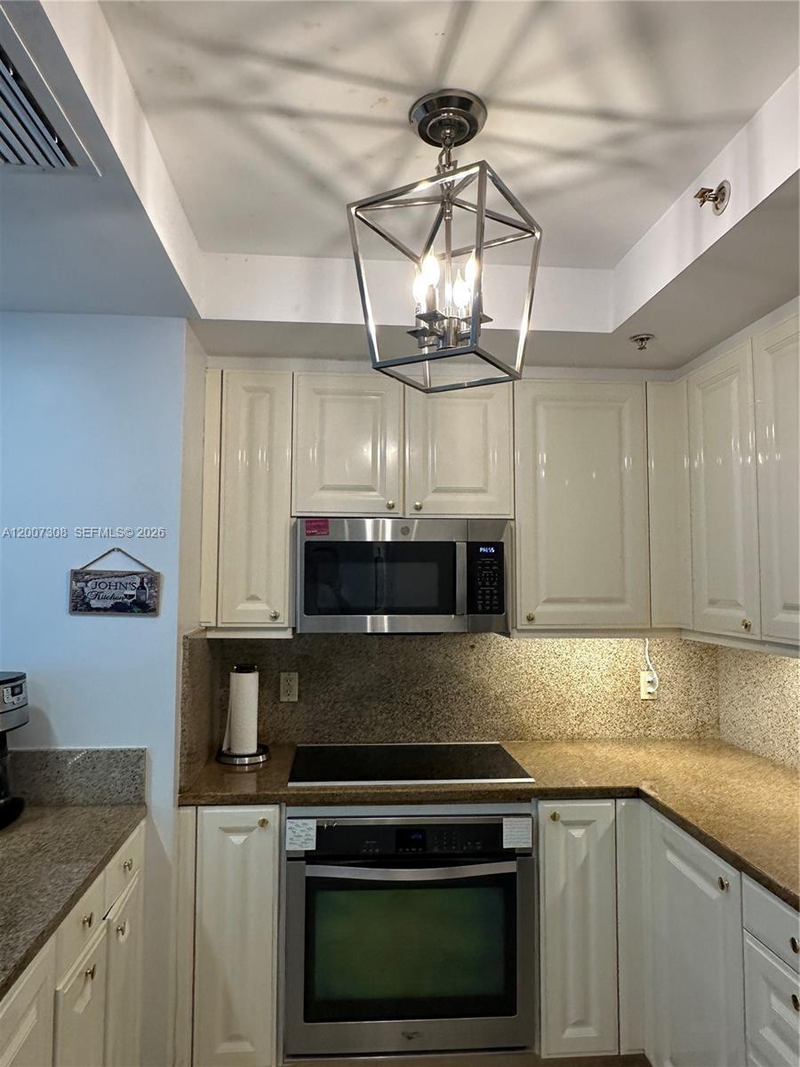 Kitchen featuring white cabinetry, stone countertops, built-in stainless steel oven, integrated microwave, and a geometric metal pendant light
