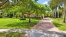 Expansive lawn featuring mature tropical landscaping, palm trees, and a paved brick driveway