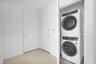 Stacked washer and dryer unit, smooth white walls, and light-toned floor tiling