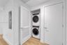 Laundry area featuring stacked front-load washer and dryer, wood-finish flooring, louvered closet door, and interior door with brushed nickel hardware