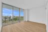 Floor-to-ceiling glass sliding doors, private balcony with metal railing, wood-finish flooring, and expansive exterior landscape