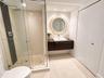 Floating dark wood-finish vanity with a rectangular vessel sink, glass-enclosed shower featuring a stone pebble floor, wall-mounted rainfall showerhea