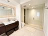 Floating wood-finish vanity with a rectangular vessel sink, frameless glass-enclosed shower featuring a stone pebble floor, and large framed mirror