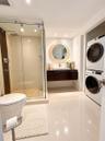 Glass-enclosed shower with a pebble-stone floor, floating dark-wood vanity, rectangular vessel sink, polished tile flooring, and integrated laundry ar