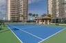 Tennis court featuring a blue surface with white boundary markings, perimeter fencing, and an open-air pavilion with a tiled roof