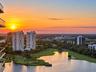 High-rise exterior featuring glass-railed balconies, overlooking a sprawling golf course, natural lake, and sunset horizon