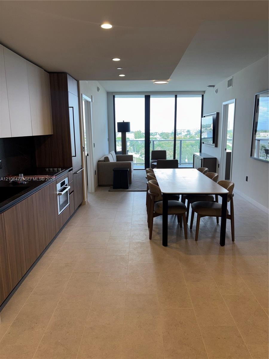 Modern kitchen featuring wood-finish cabinetry, built-in stainless steel oven, stone-surface countertops, recessed ceiling lighting, and floor-to-ceil