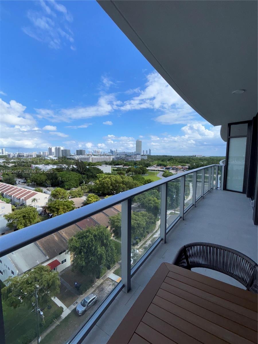 Covered balcony featuring a sleek glass railing and expansive urban and canopy scenery