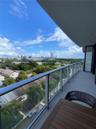 Covered balcony featuring a sleek glass railing and expansive urban and canopy scenery