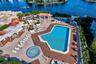 Waterfront pool deck featuring an expansive pool, a circular spa, a covered pavilion with wood-beam construction, and extensive concrete hardscaping