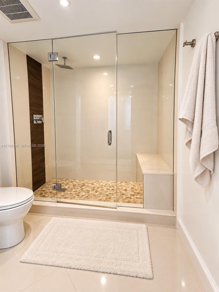 Walk-in shower featuring a frameless glass enclosure, pebble-stone flooring, integrated built-in bench, rain-style showerhead, and dark wood-tone vert