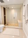 Walk-in shower featuring a frameless glass enclosure, pebble-stone flooring, integrated built-in bench, rain-style showerhead, and dark wood-tone vert
