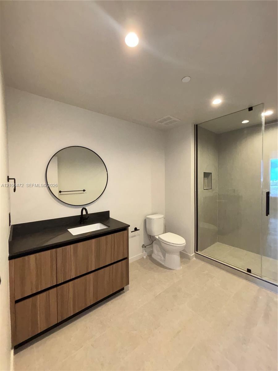 Bathroom featuring a wood-finish floating vanity with a dark countertop and integrated sink, circular wall-mounted mirror, matte black faucet, and a w
