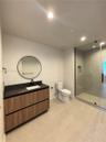 Bathroom featuring a wood-finish floating vanity with a dark countertop and integrated sink, circular wall-mounted mirror, matte black faucet, and a w