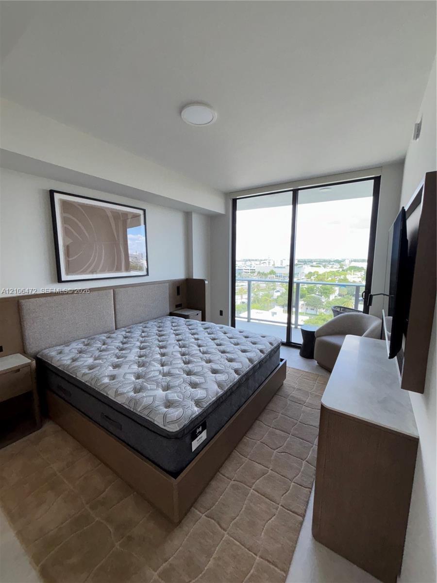 Floor-to-ceiling glass sliding doors, built-in wooden headboard with integrated side tables, and balcony with metal railing