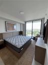 Floor-to-ceiling glass sliding doors, built-in wooden headboard with integrated side tables, and balcony with metal railing