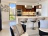Contemporary kitchen featuring wood-finish cabinetry, a white waterfall-edge island, built-in stainless steel appliances, and glass pendant lighting