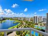 Elevated balcony featuring a white railing, overlooking an expansive lake, golf course fairways, and tennis courts
