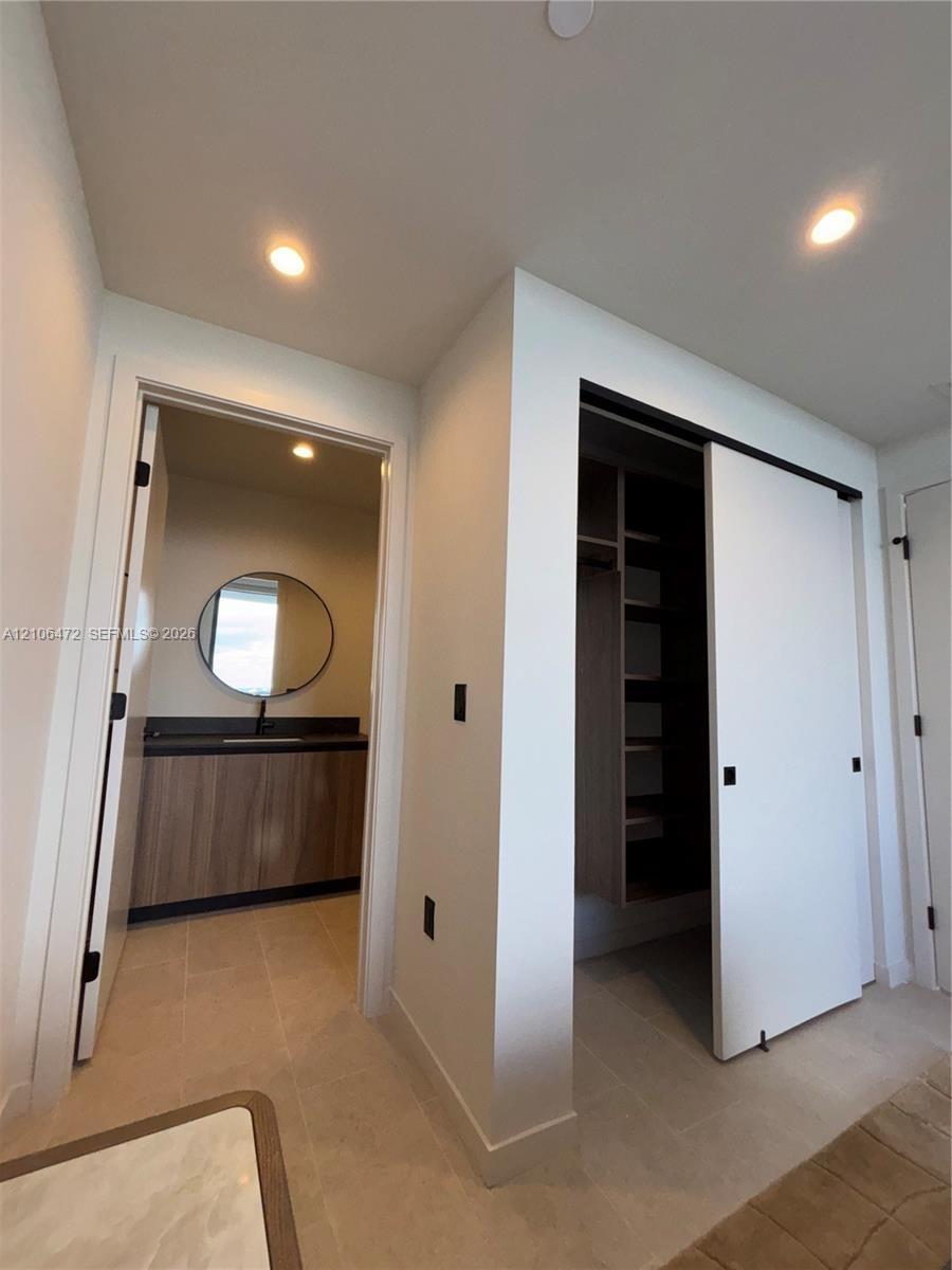 Built-in closet with sliding doors and custom shelving, vanity featuring a rectangular vessel sink and wood-finish cabinetry, circular wall-mounted mi