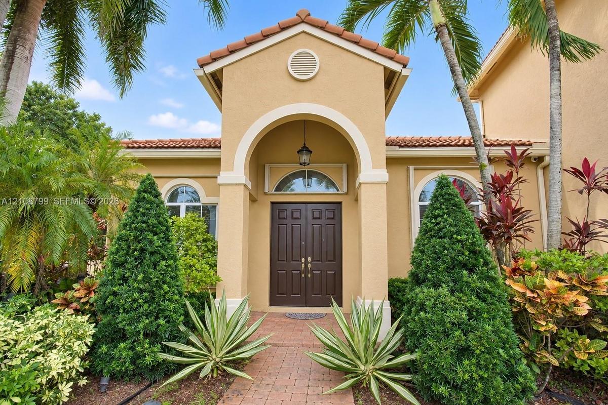 Stucco exterior featuring a covered portico entrance, arched entryway, double-door main entry, and clay tile roof