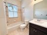Bathroom featuring a dark wood-finish vanity with a white countertop and integrated sink, a tiled tub-shower combination, ceramic tile flooring, and a