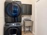 Stacked laundry unit, dark-finish cabinetry, and stainless steel utility sink with gooseneck faucet