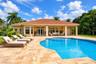 Stucco exterior featuring a tiled hip roof, expansive stone paver pool deck, covered patio, and custom-shaped swimming pool