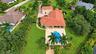 Expansive property featuring a multi-level structure with a terracotta tile roof, a stone-paved patio, a custom-shaped swimming pool, and mature palm 