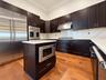 Kitchen featuring dark-finish cabinetry, stone-style countertops, stainless steel appliances, a center island with built-in microwave, and wood-finish