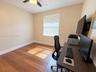 Wood-finish flooring, neutral wall tones, window with horizontal blinds, and a ceiling fan with integrated lighting