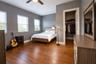 Room featuring wood-finish flooring, three windows with integrated blinds, and a built-in walk-in closet with overhead shelving and hanging rods