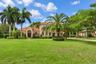 Stucco exterior with an arched entryway, terracotta tile roof, and expansive manicured lawn featuring mature palm trees