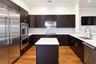 Kitchen featuring dark wood cabinetry, a central island with a stone countertop, stone slab backsplash, stainless steel appliances, and wood-finish fl