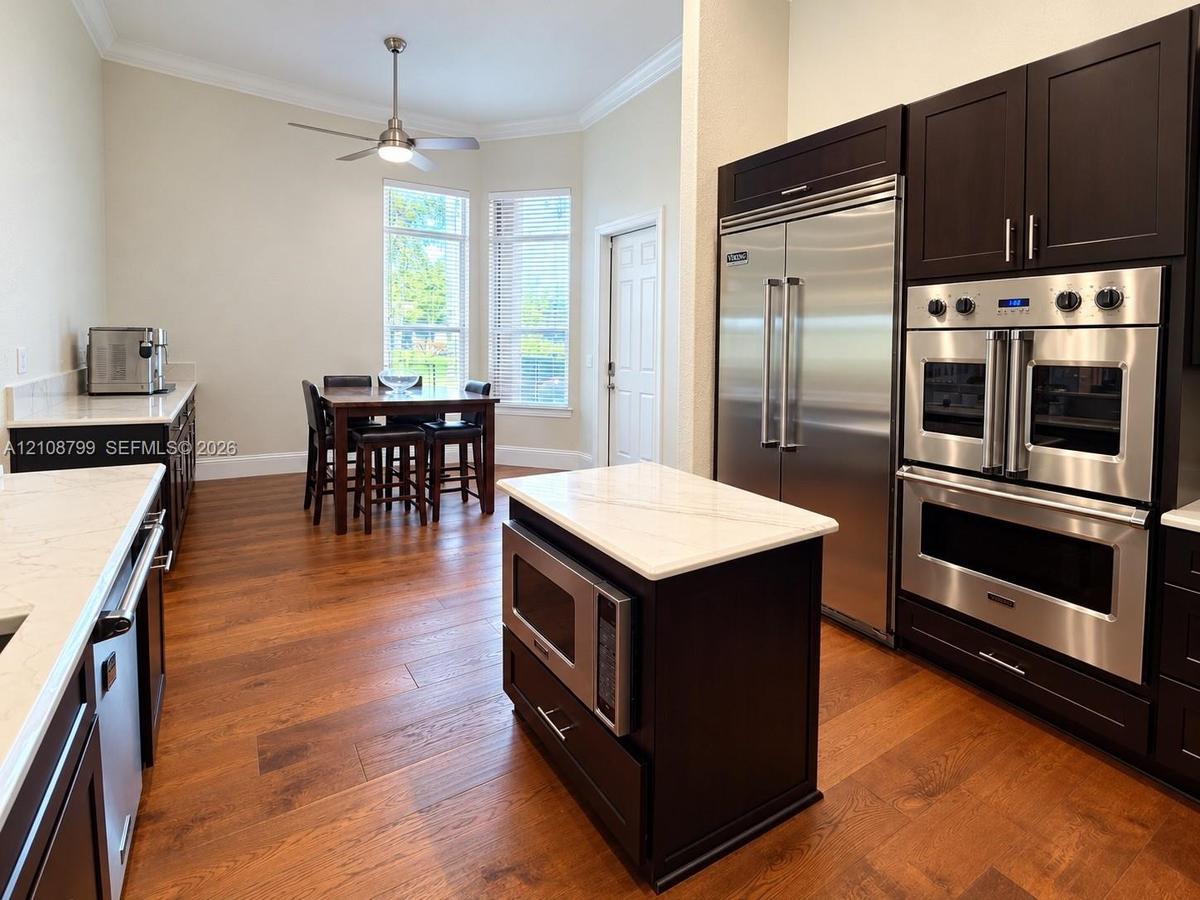 Kitchen featuring dark cabinetry, stone-finish countertops, stainless steel professional-grade double wall ovens, a side-by-side refrigerator, and woo