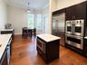 Kitchen featuring dark cabinetry, stone-finish countertops, stainless steel professional-grade double wall ovens, a side-by-side refrigerator, and woo