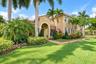 Stucco exterior featuring a tiled roof, arched entryway, and manicured landscaping with mature palm trees and a paved walkway