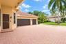 Paver driveway, three-car garage, stucco exterior, clay tile roof, and mature palm landscaping