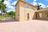 Stucco exterior featuring an expansive paved driveway, a multi-level roofline with clay tile detailing, exterior wall-mounted lighting, and integrated