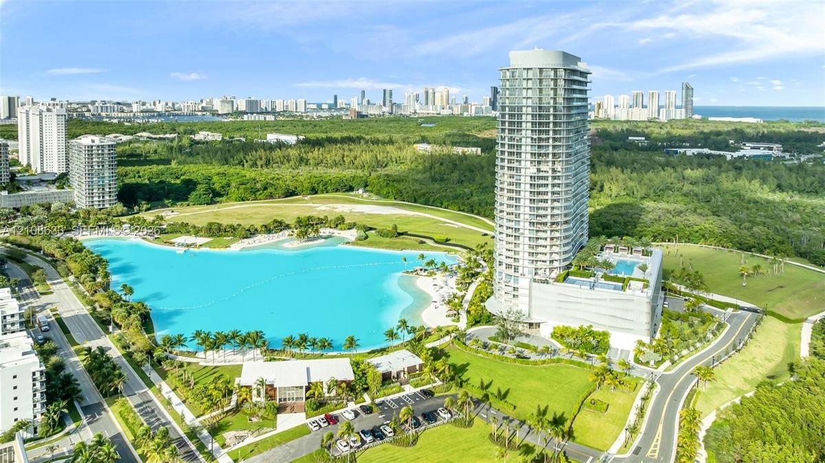 High-rise residential tower featuring an expansive turquoise lagoon, manicured grounds, a podium-level swimming pool, and proximity to coastal terrain