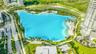 Large-scale crystalline lagoon featuring a sandy shoreline, palm-lined perimeter, paved walkways, and expansive landscaped grounds