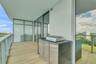 Covered balcony featuring wood-finish tile flooring, glass railings, and a built-in outdoor kitchen with stainless steel cabinetry and a metal grill